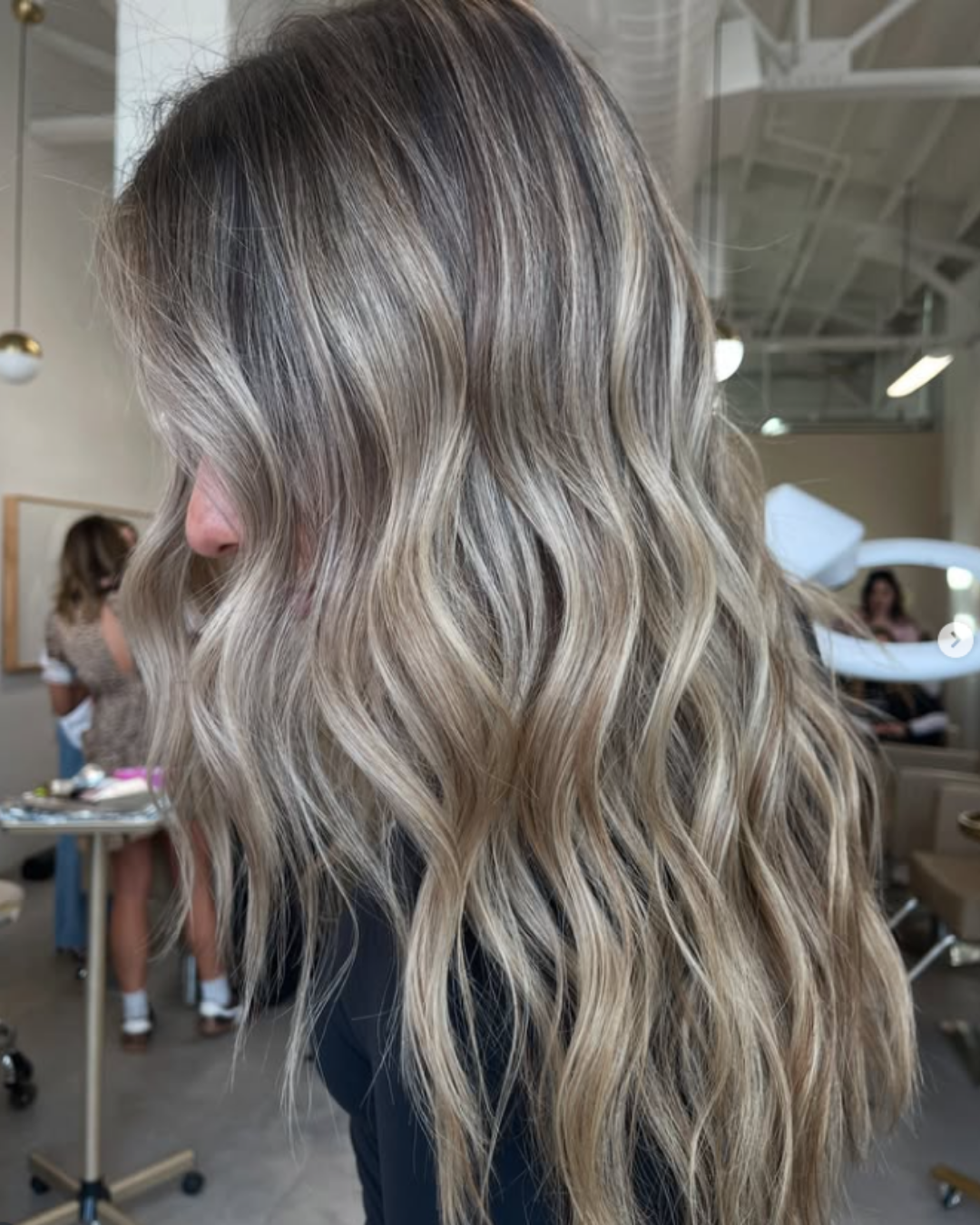 Side profile of long wavy blonde balayage with a seamless transition from dark roots by Maggie.