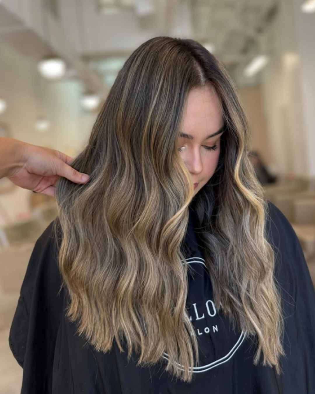 Long, wavy bronde hair featuring a blend of brown and blonde tones for a lived-in look by Brianna.