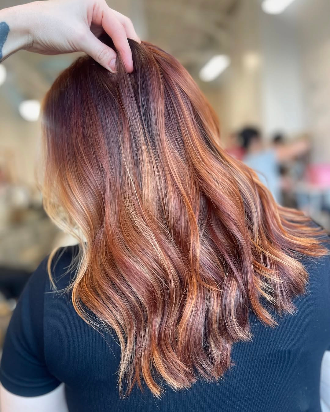 Back view of vibrant copper balayage with dimensional red tones and soft waves by Maggie.