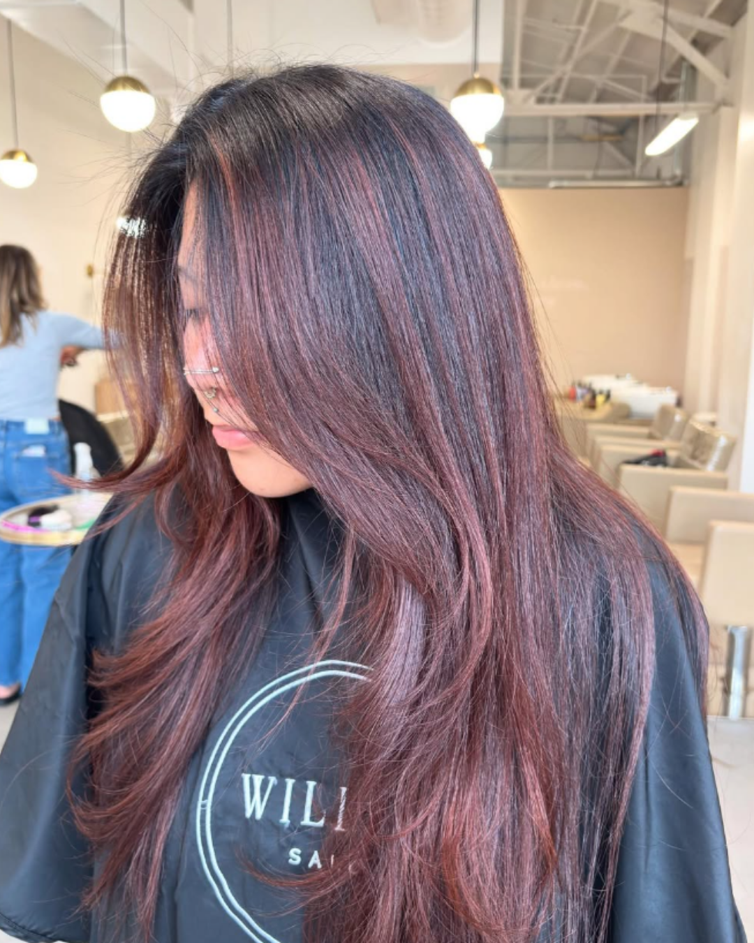 Long, layered dark hair with rich copper brown balayage highlights and face-framing layers by Gel.