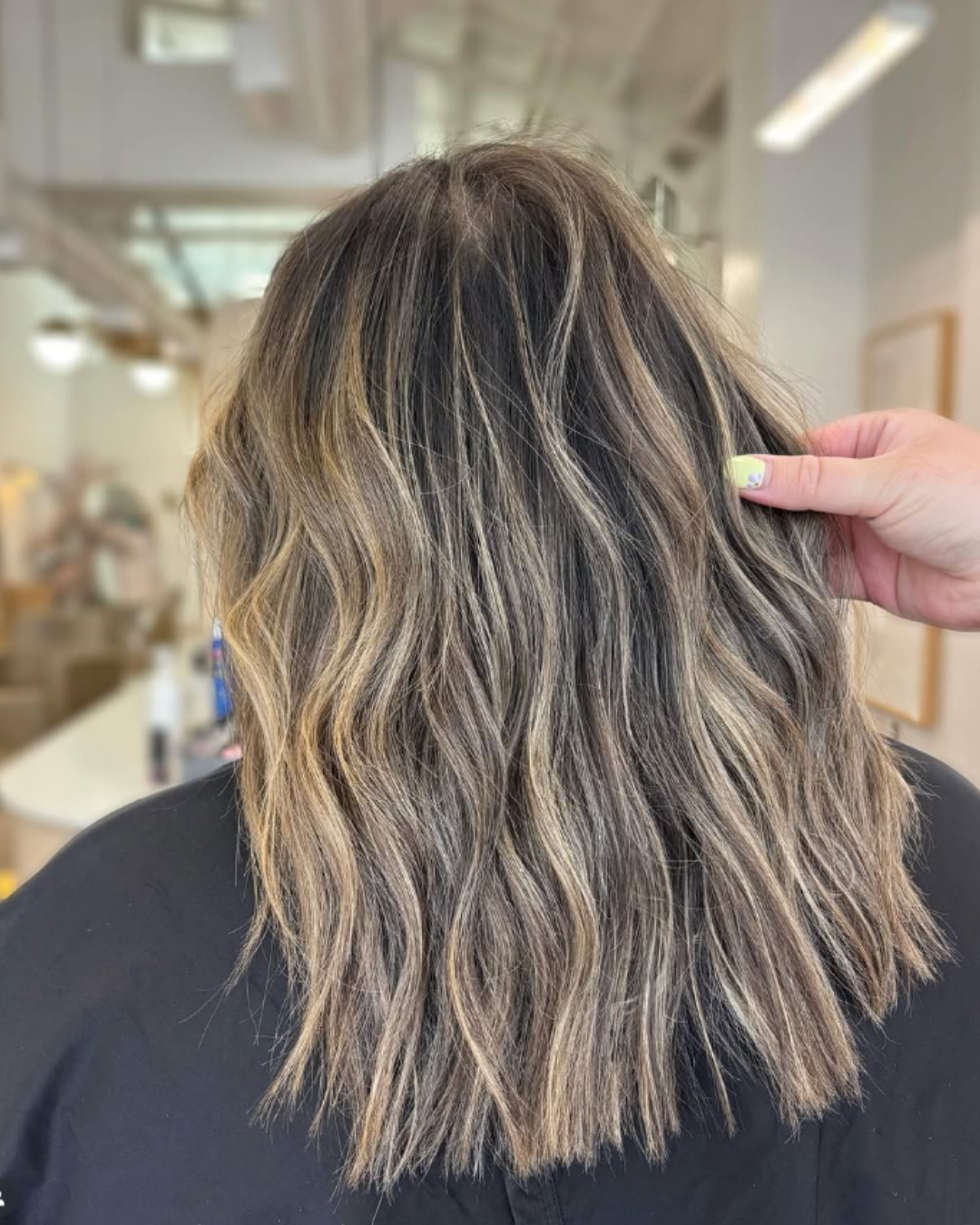 Back view of a wavy bob featuring dimensional caramel blonde highlights on dark hair by Jules.