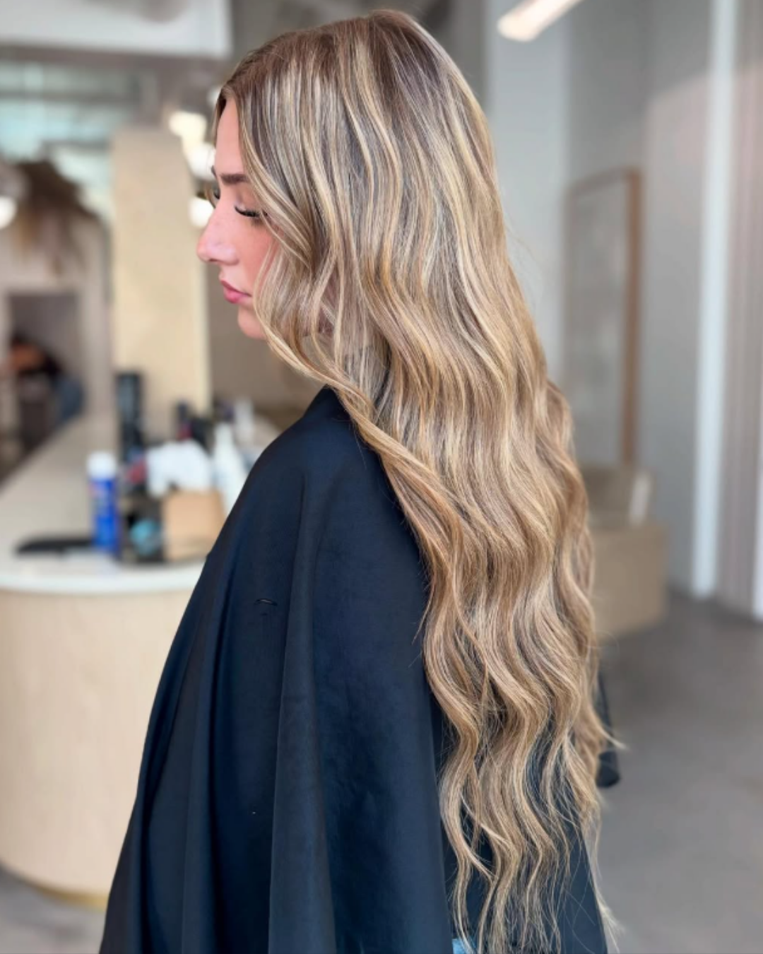 Side profile of long, wavy honey blonde hair blended with 22-inch hair extensions by Gel.