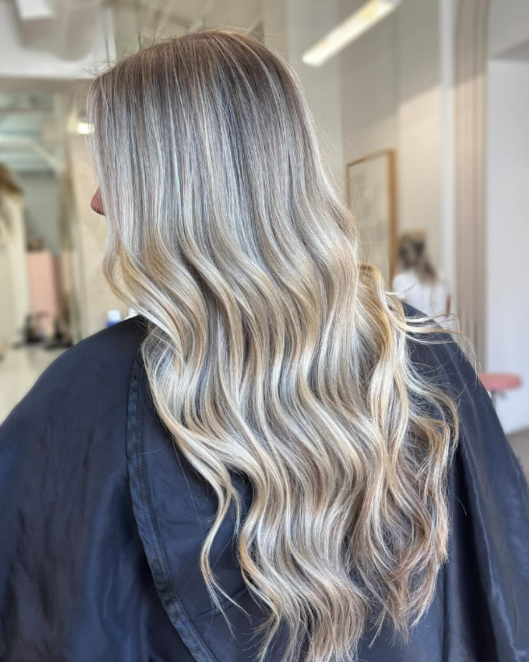 Long and wavy hair featuring a sunkissed dimensional blonde balayage with cool and warm tones by Jules.