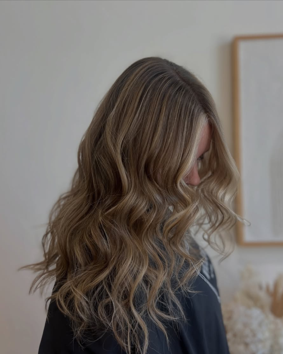 Side view of long wavy hair with a blended blonde balayage and light face-framing money piece by Desirae