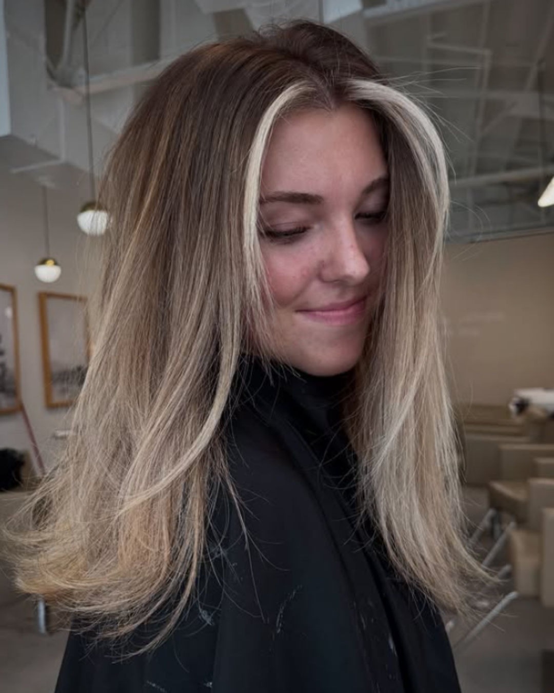 Woman with lived-in blonde hair showing dark roots, bright blonde ends, and a bold face-framing money piece by Brittany