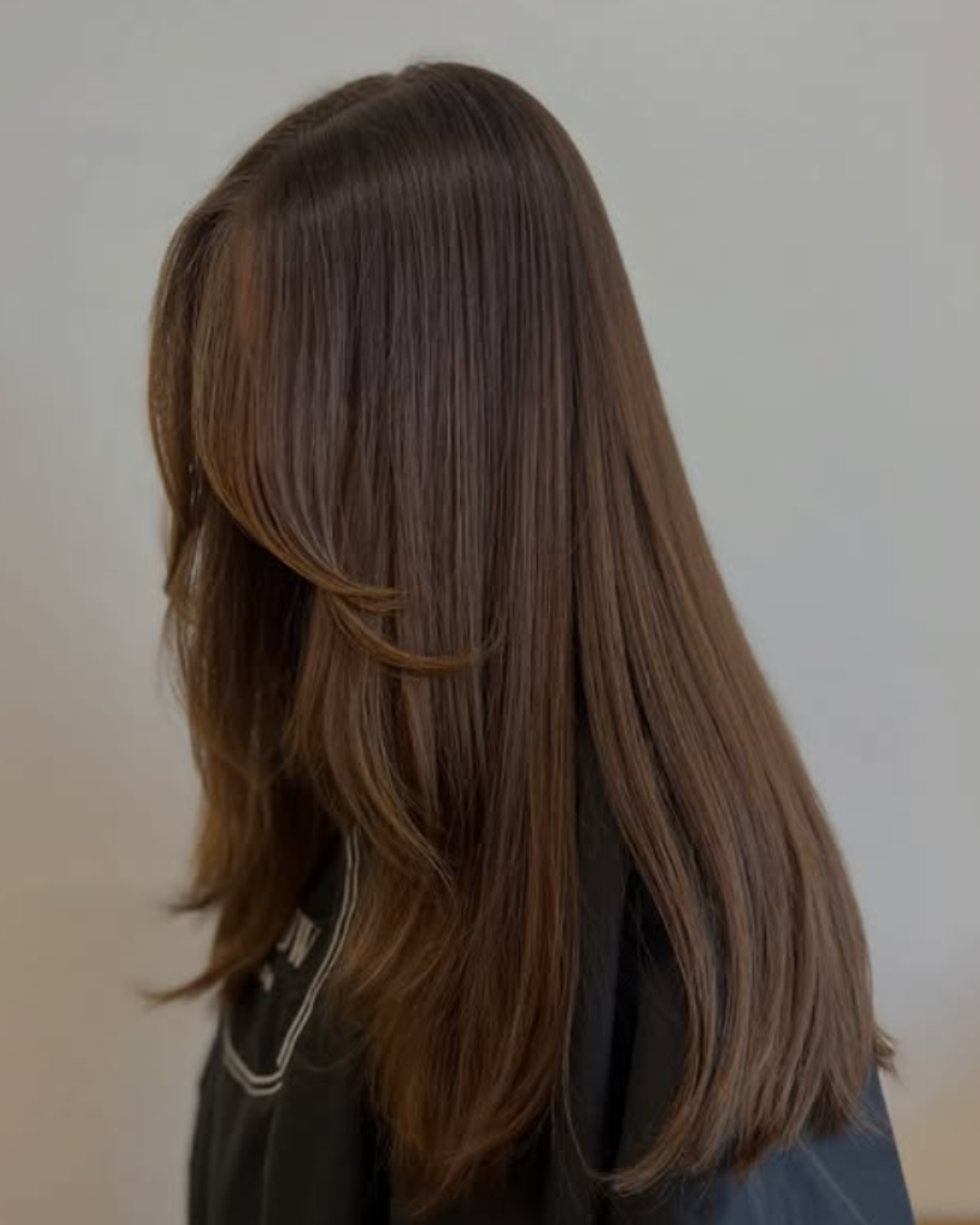 Side profile of sleek long auburn brown hair with face-framing layers and soft curtain bangs by Desirae