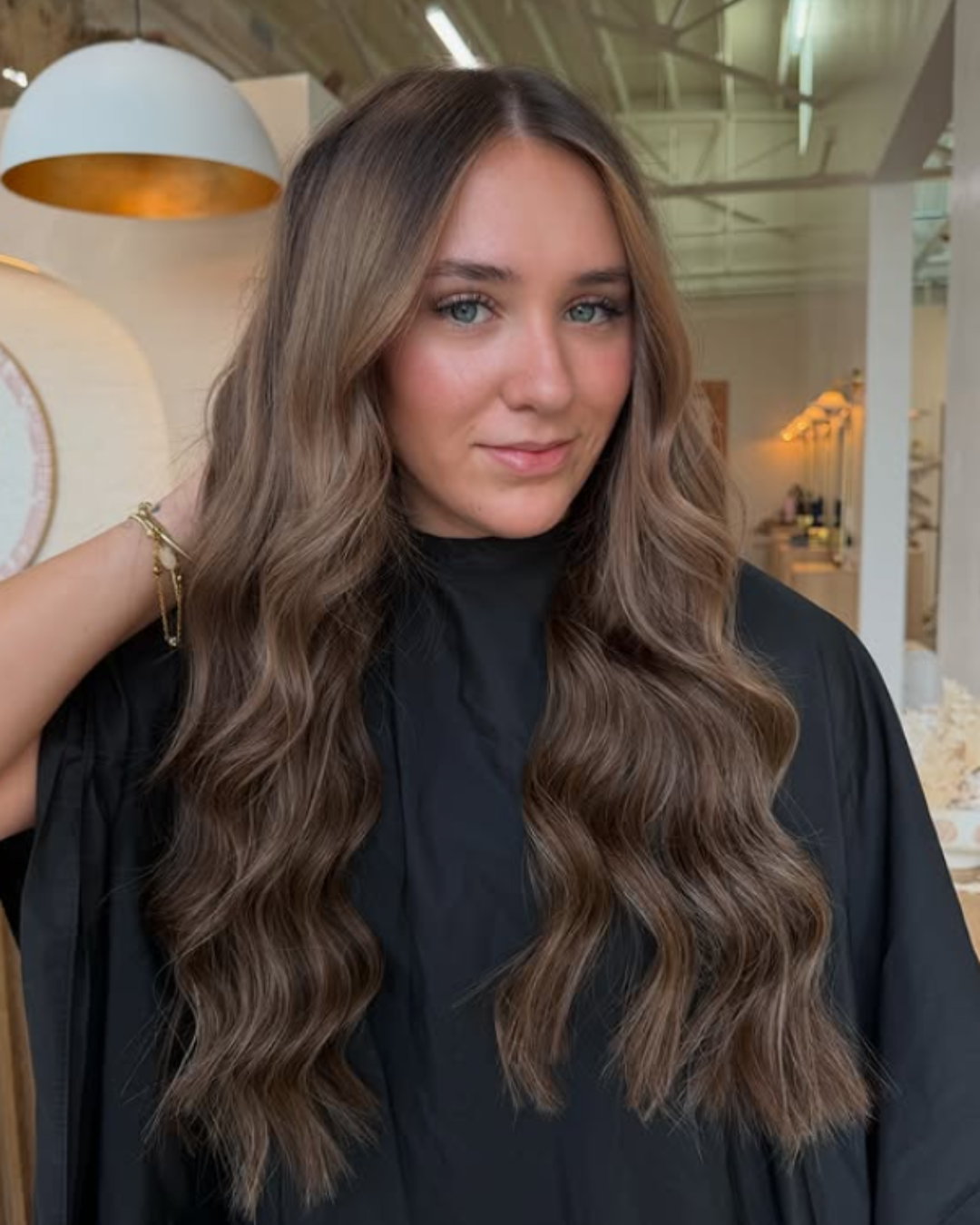 Woman showing off long, soft wavy light-brown hair extensions with natural volume and shine by Britttany