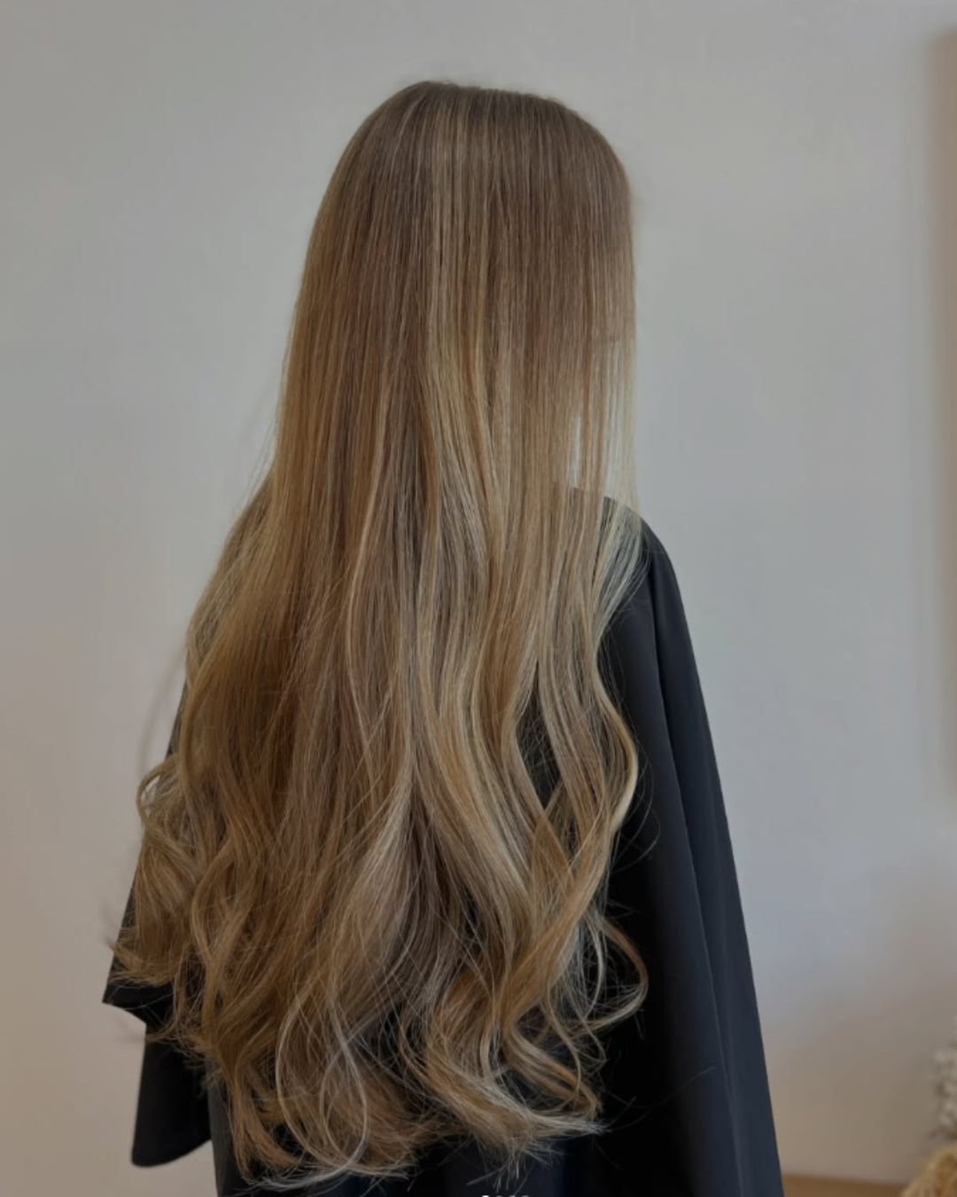 Back view of long, straight ash blonde hair featuring full highlights and soft loose curls at the ends by Desirae