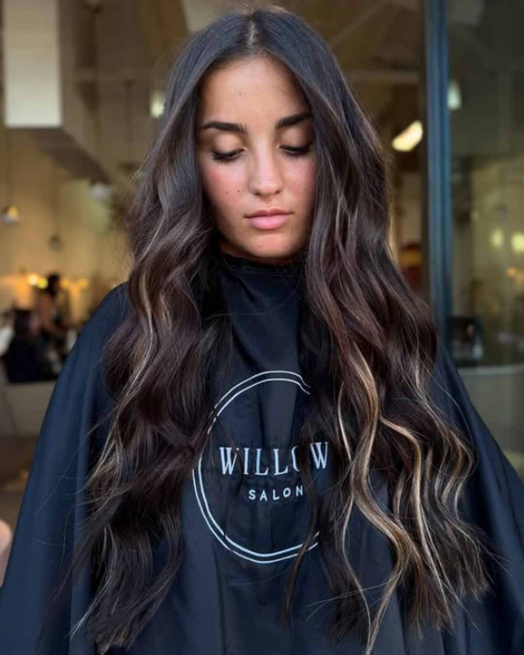 Woman with long dark brown hair styled in loose waves with subtle blonde highlights from K-tip extensions by Brittany.