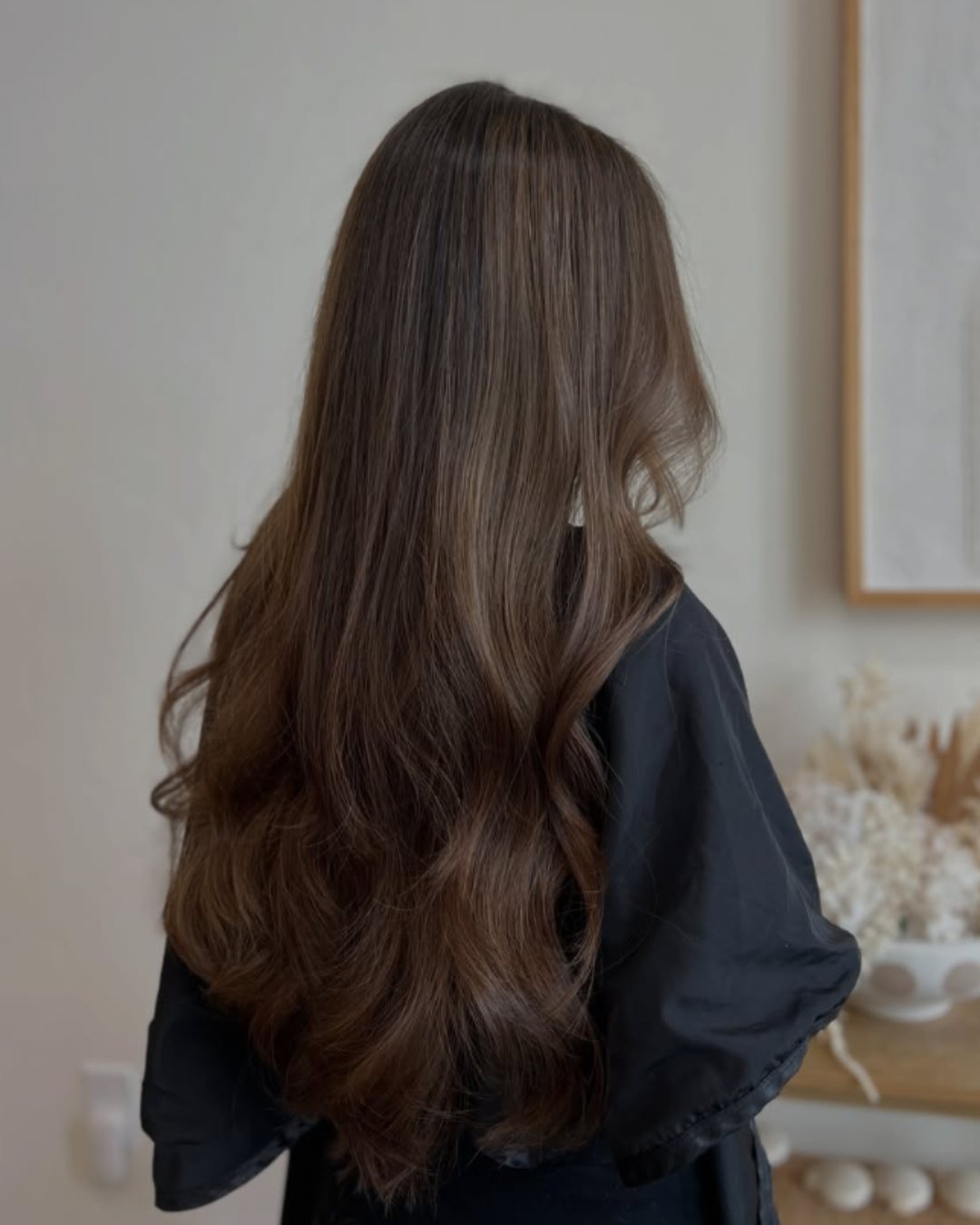 Rear view of long, flowing dark brown hair styled in soft, voluminous waves with subtle sunkissed tones by Desirae